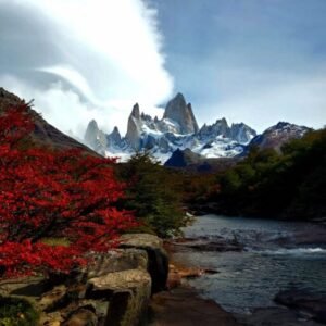 Cerro Fitzroy with snow-capped peaks, surrounded by red autumn foliage and a clear stream in Patagonia.