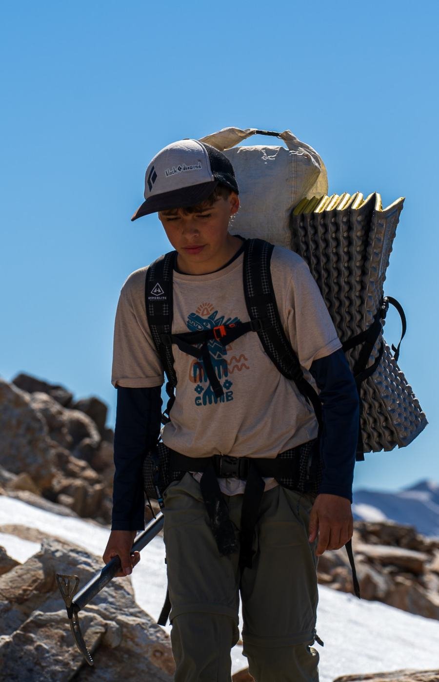 Hiker carrying a loaded backpack and sleeping mat on rocky terrain